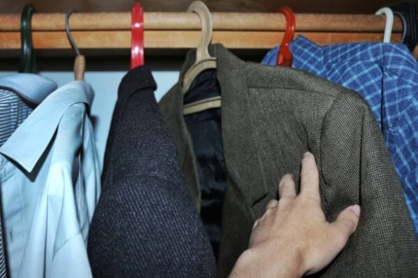 Hand reaching for a classic blazertje in a wardrobe among other clothes