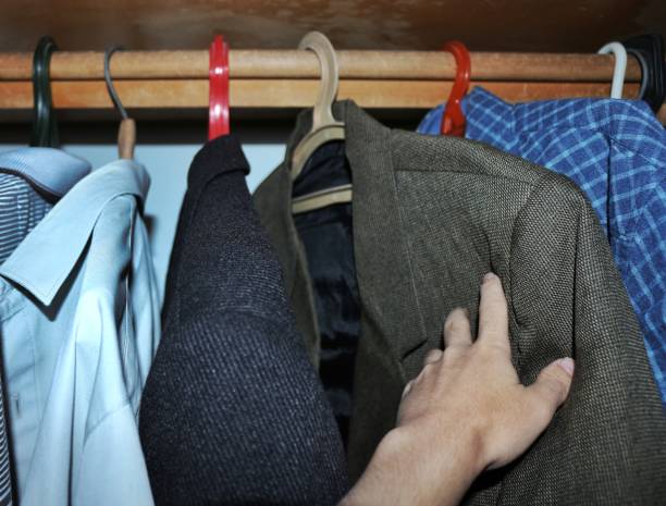 Hand reaching for a classic blazertje in a wardrobe among other clothes