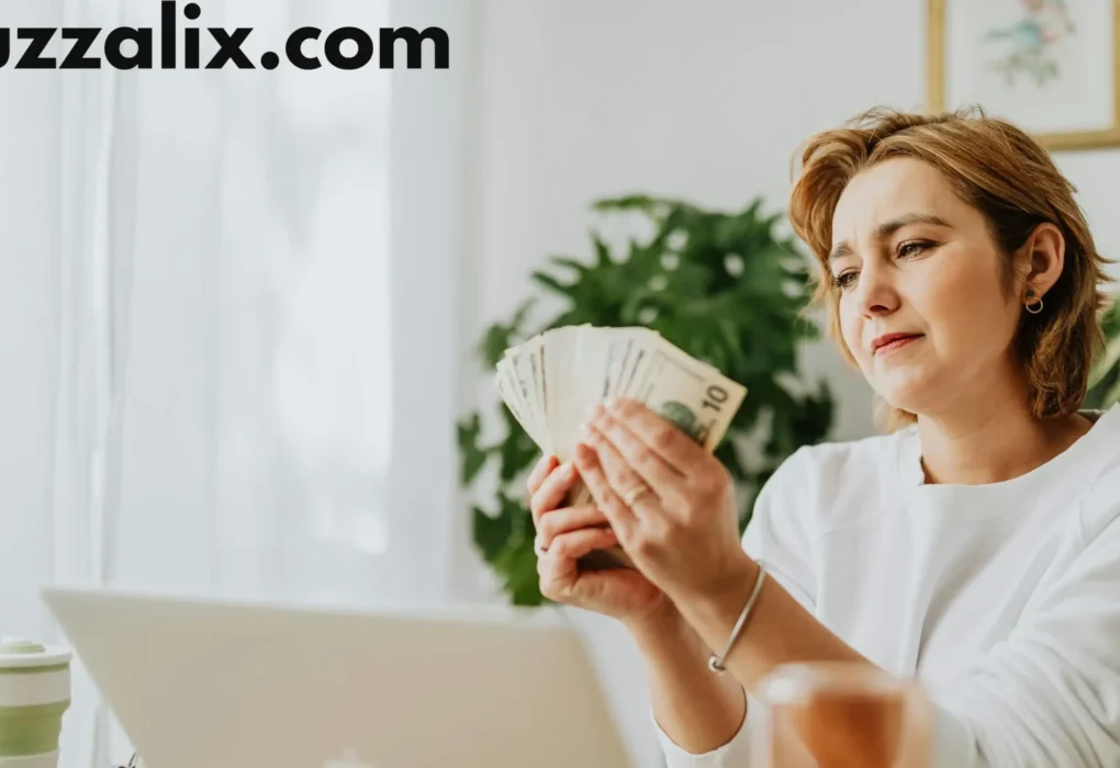A woman sitting at her desk with a laptop, counting money while researching tech salaries, representing income growth in the 2025 Tech Salary Guide by Buzzalix.