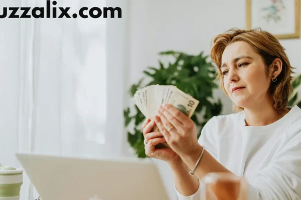 A woman sitting at her desk with a laptop, counting money while researching tech salaries, representing income growth in the 2025 Tech Salary Guide by Buzzalix.